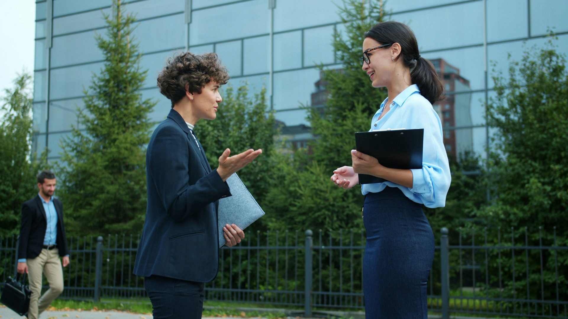 Zwei Geschäftsfrauen unterhalten sich vor einem modernen Bürogebäude.